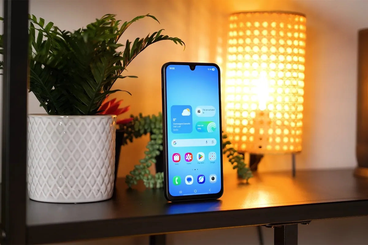 Samsung Galaxy A17 staat rechtop op een plank naast een witte plantenpot en een sfeervolle tafellamp