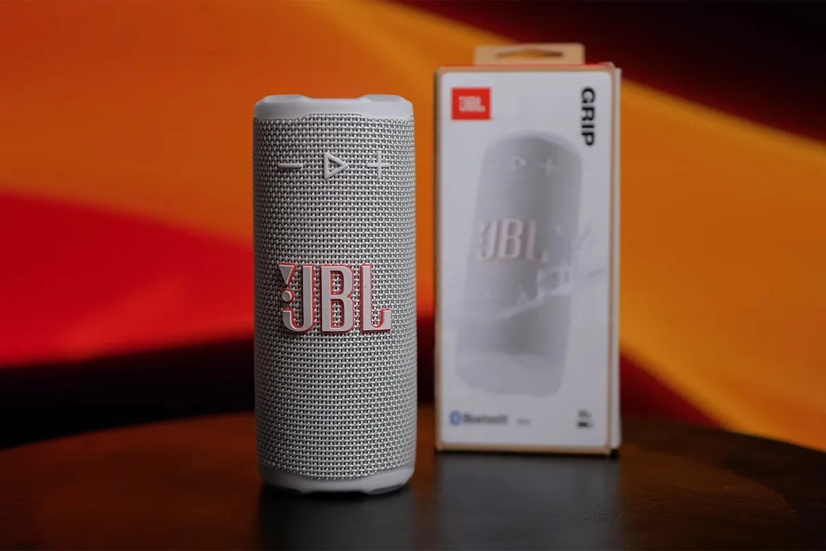 Close-up van de JBL Grip-speaker en zijn verpakking op een oranje achtergrond.