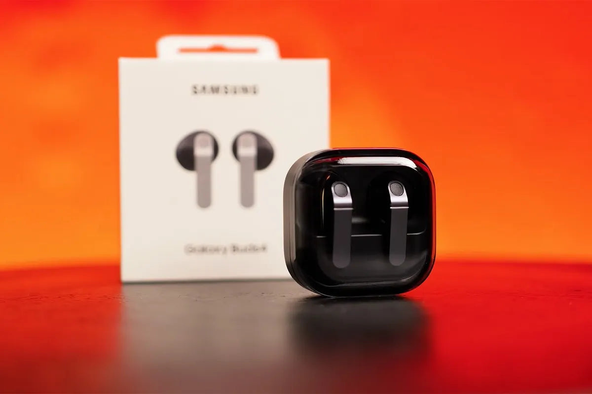 Samsung Galaxy Buds 4 in de oplaadcase met het verpakkingsdoosje en een oranje muur vaag op de achtergrond.