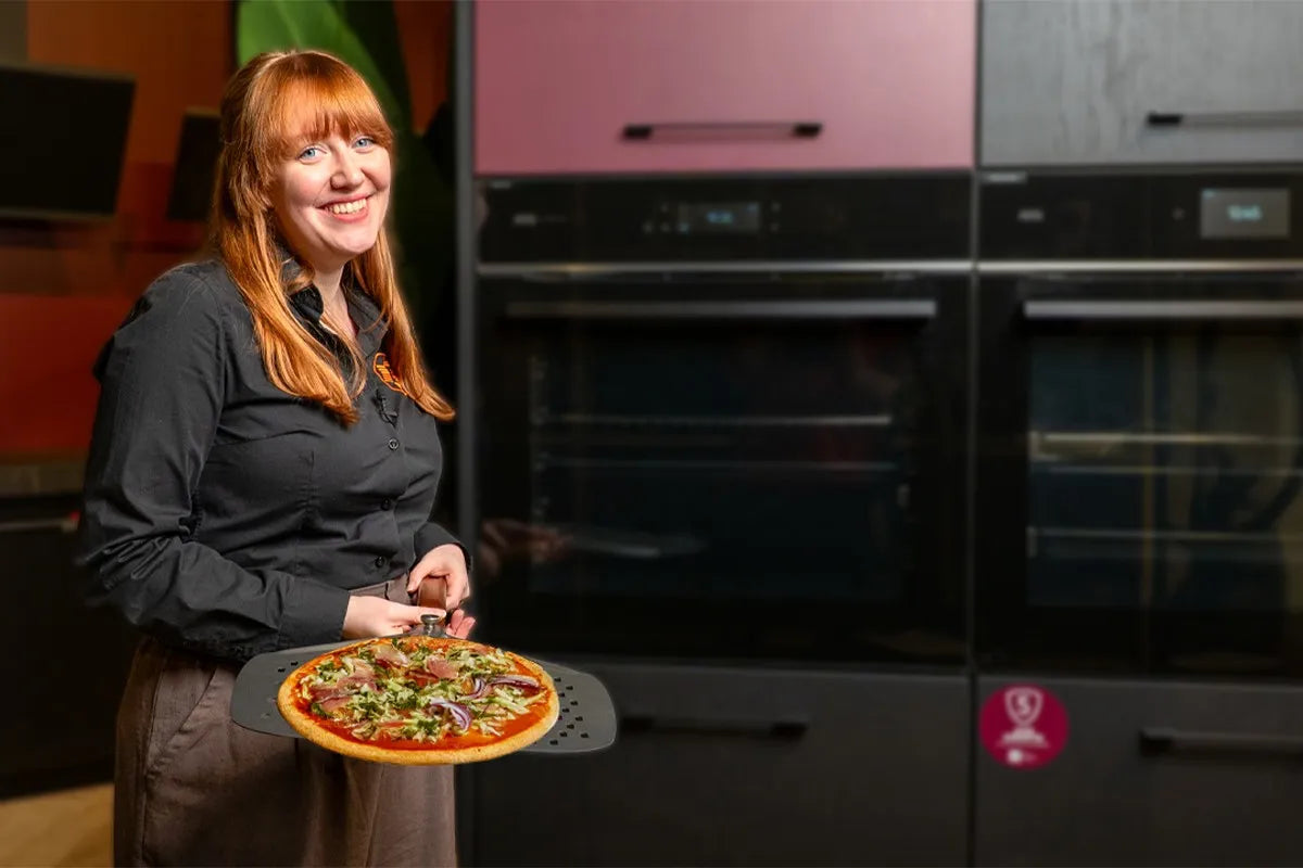 Persoon op voorgrond met pizza op pizzaschep.