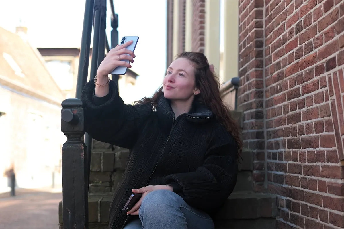 Persoon zit op een stenen trap en neemt een selfie met de Samsung Galaxy S26.