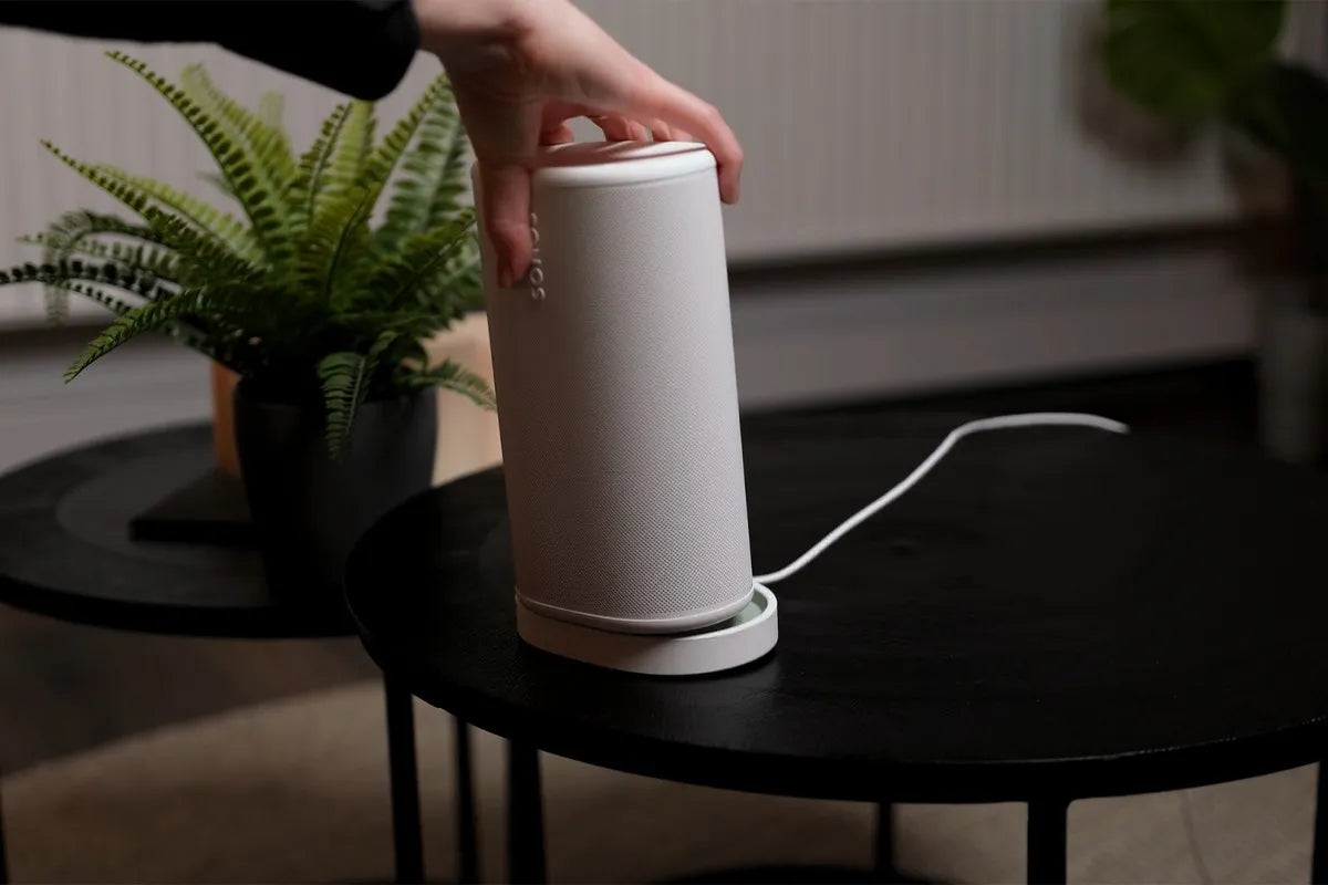 Sonos Play in witte uitvoering wordt door een persoon in het oplaadstation gezet.