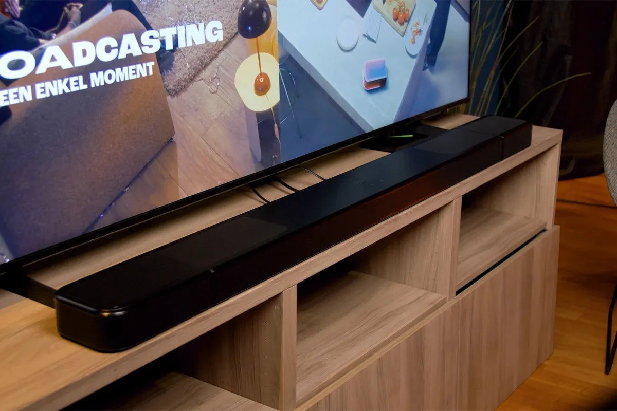 De JBL Bar 1300MKII soundbar strak gepositioneerd op een houten tv-meubel onder een grote televisie.