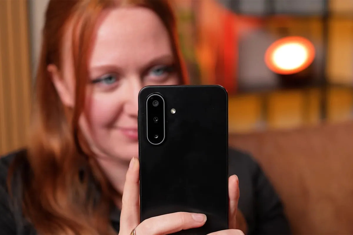 Een vrouw houdt een Samsung Galaxy A17-smartphone voor zich, met de achterkant naar de camera gericht; de telefoon heeft drie verticale cameralenzen en een LED-flitser in een ovale cameramodule