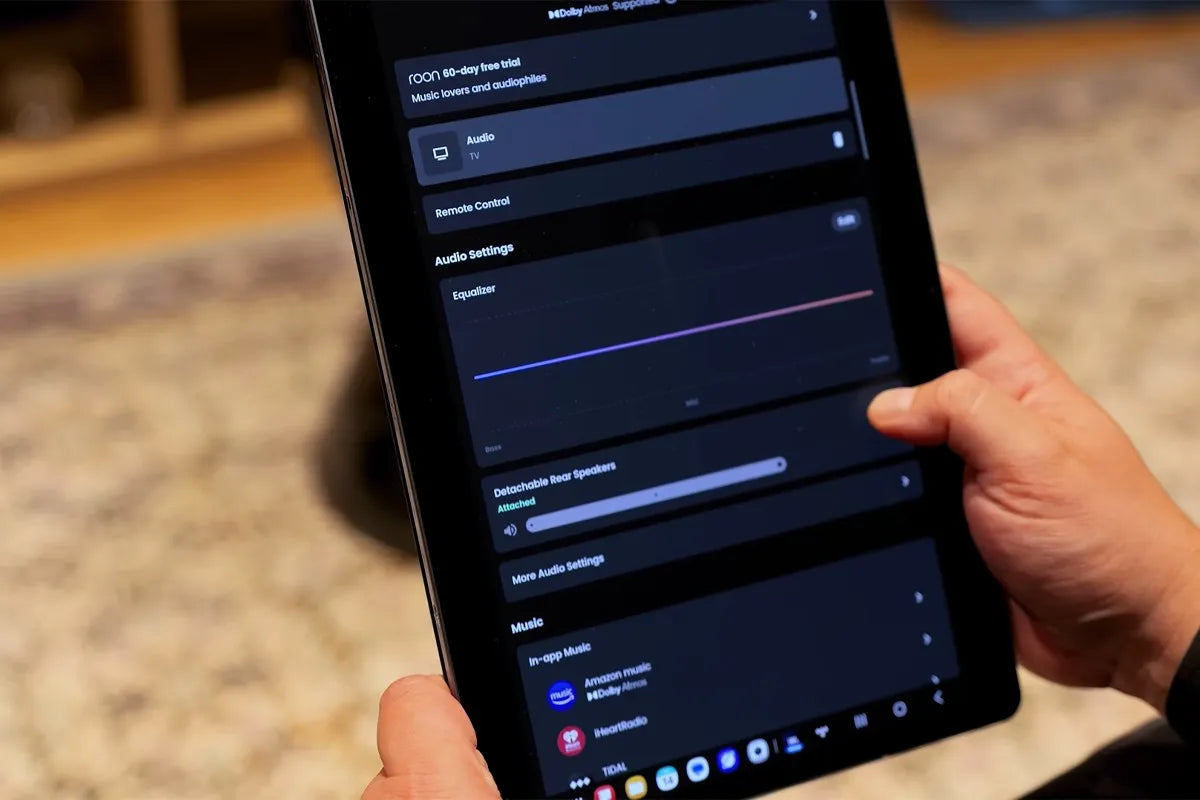 Een persoon houdt een tablet vast en bekijkt de geluidsinstellingen van een JBL-audiosysteem via een app.