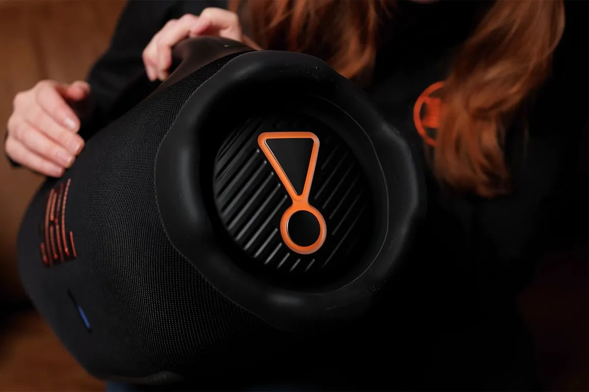 Persoon houdt JBL Boombox 4 vast waarbij zijkant zichtbaar is met grote bass en kenmerkende uitroepteken.