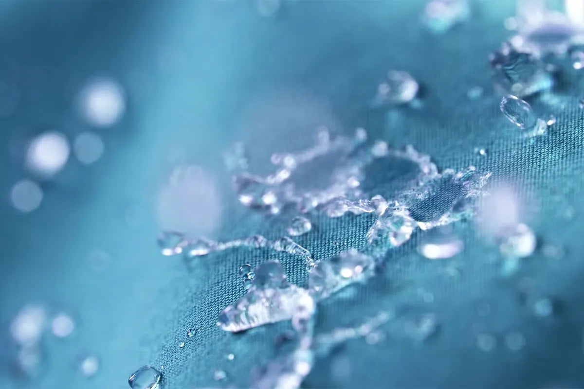 Een close-up van waterdruppels die op een blauwe waterafstotende stof liggen, wat erop wijst dat het oppervlak geïmpregneerd is en geen vocht doorlaat