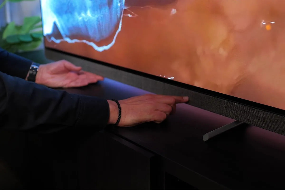 Een persoon wijst met beide handen naar de stoffen speakerafwerking aan de onderkant van het scherm van de Philips OLED+