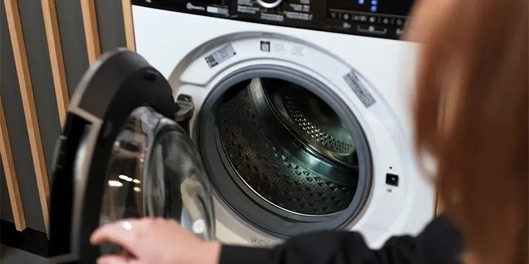 Een vrouw opent de deur van een Whirlpool-wasmachine; het display toont een resterende wastijd van 2:30 uur en de binnenkant van de trommel is goed zichtbaar met een karakteristiek patroon op het metaal.