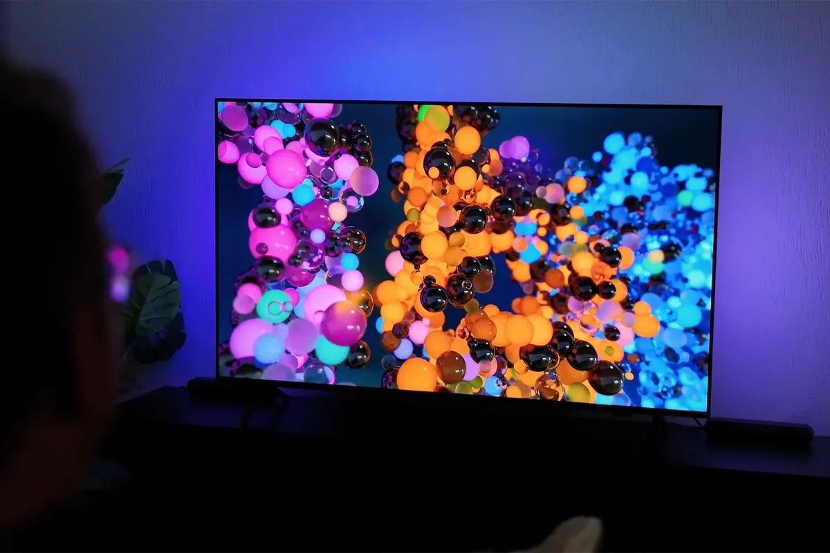 Persoon kijkt naar een tv in een donkere kamer met daarop kleurige bolletjes die het effect van Ambilight goed naar voren laten komen.