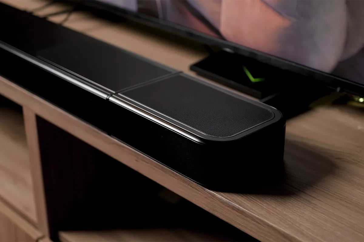 De JBL Bar 1300MKII staat op een houten tv-meubel direct onder een televisie. De soundbar heeft afgeronde hoeken en een matzwarte metalen grill.